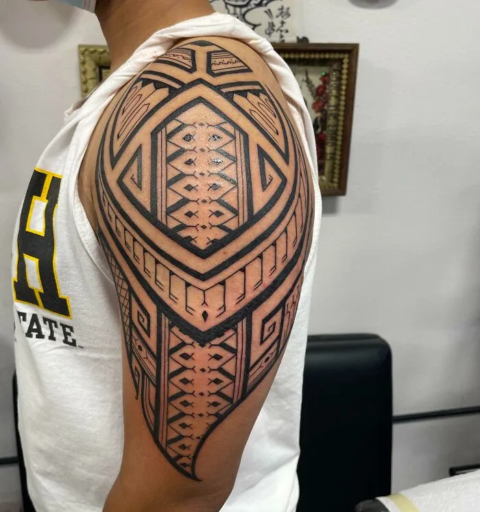 A detailed tribal tattoo design on an upper arm, featuring intricate geometric patterns.