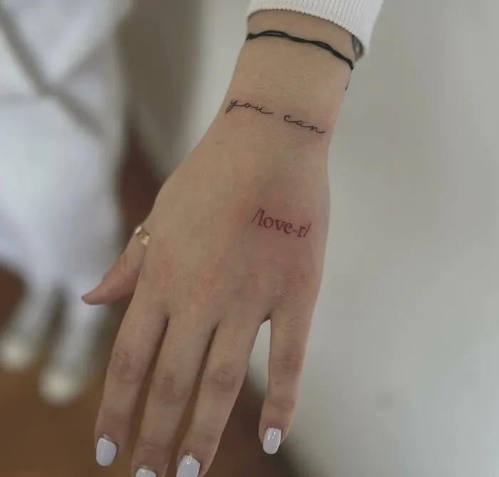 Close-up of a hand with small tattoos reading "you can" and "/love it" showing creative small hand tattoo design.