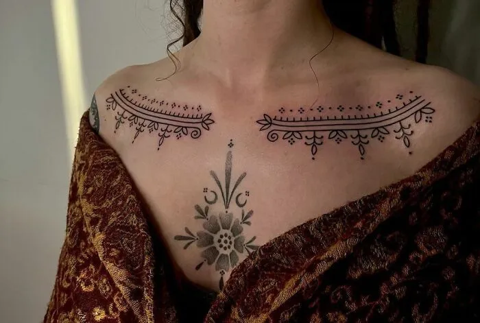Intricate collarbone tattoos featuring elegant floral designs on a woman's upper chest, wrapped in a patterned shawl.