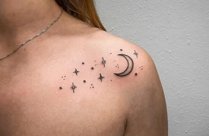 Minimalist moon and stars collarbone tattoo on a woman's shoulder.
