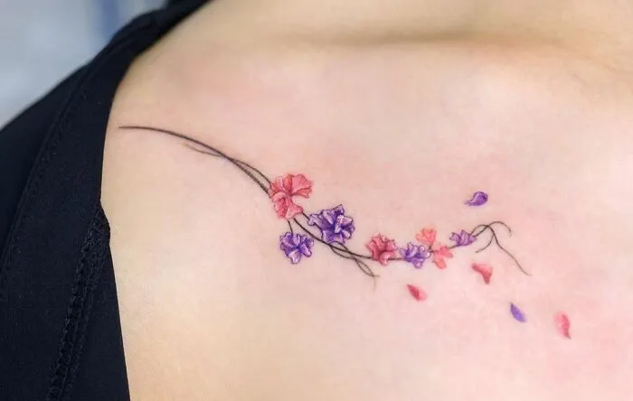 Floral collarbone tattoo with pink and purple blossoms on a person's shoulder.