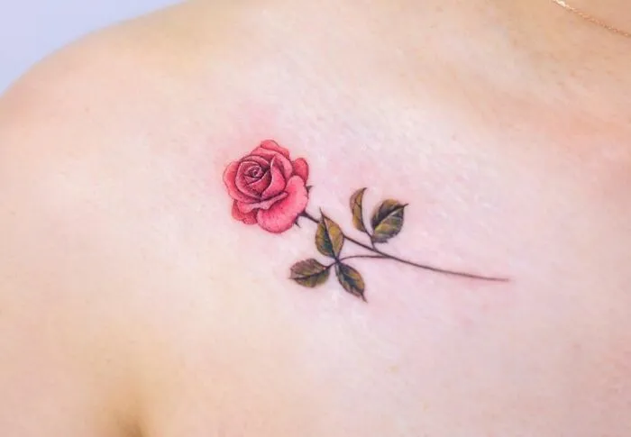 Rose tattoo on collarbone with delicate leaves, showcasing stunning design for men and women.