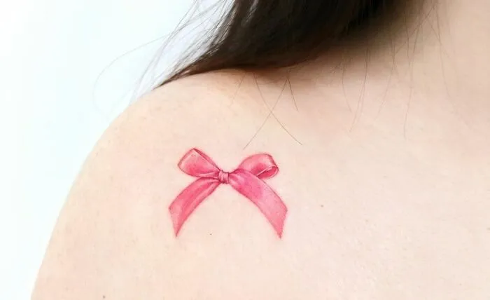 Pink bow collarbone tattoo on person, showcasing stylish body art for men and women.