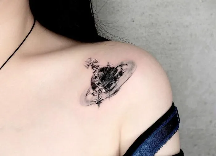 Collarbone tattoo of a planet with rings and stars, inked on someone's shoulder.