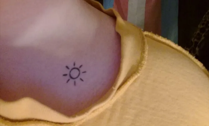 Minimalist sun collarbone tattoo on a person wearing a yellow top.