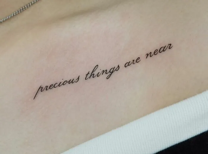 Elegant script collarbone tattoo on skin, reading "precious things are near," showcasing minimalist design for men and women.