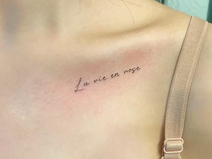 Collarbone tattoo with elegant script reading "La vie en rose" on a woman's skin.