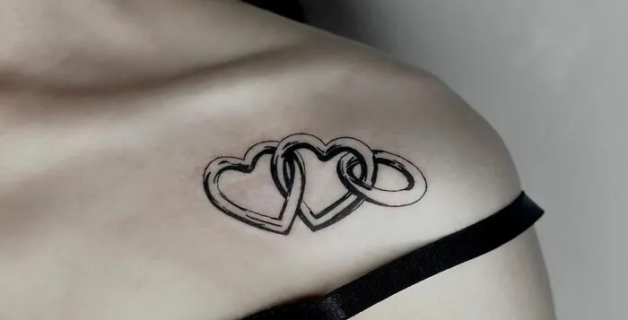 Collarbone tattoo of interlinked hearts and rings on a person's shoulder.