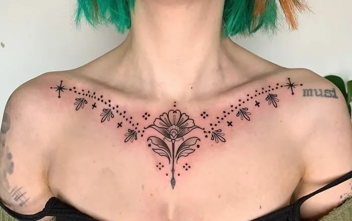 Intricate collarbone tattoo design on woman with green hair.