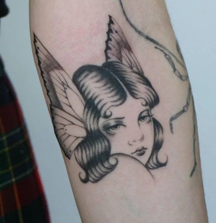 Black ink butterfly tattoo with a woman's face on an arm, showcasing intricate details and artistic design.