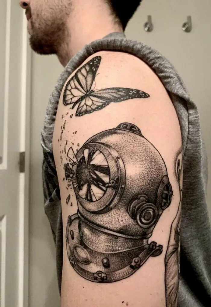 Arm with detailed butterfly tattoo next to a vintage diving helmet design.