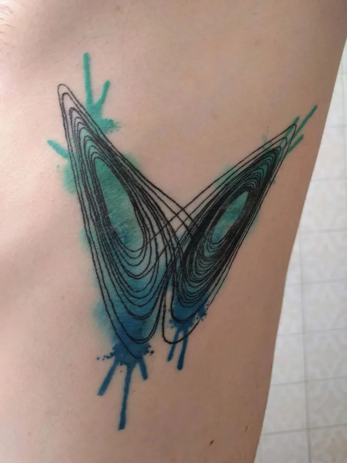 Abstract butterfly tattoo with teal splashes, resembling colorful butterfly wings.