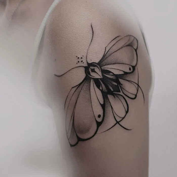 Black ink butterfly tattoo on upper arm, showcasing elegant and intricate design.