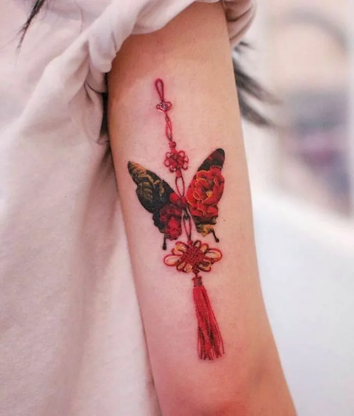 Colorful butterfly tattoo with floral patterns and tassel on forearm.