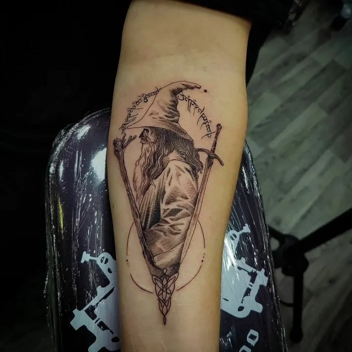 "Detailed Gandalf tattoo design on forearm from Lord of the Rings series, featuring elvish script and staff."