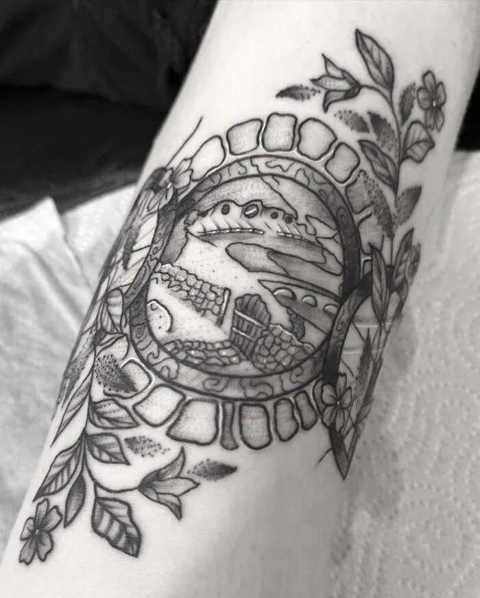 Black and grey tattoo of a Hobbit hole from Lord of the Rings, surrounded by leaves and flowers.