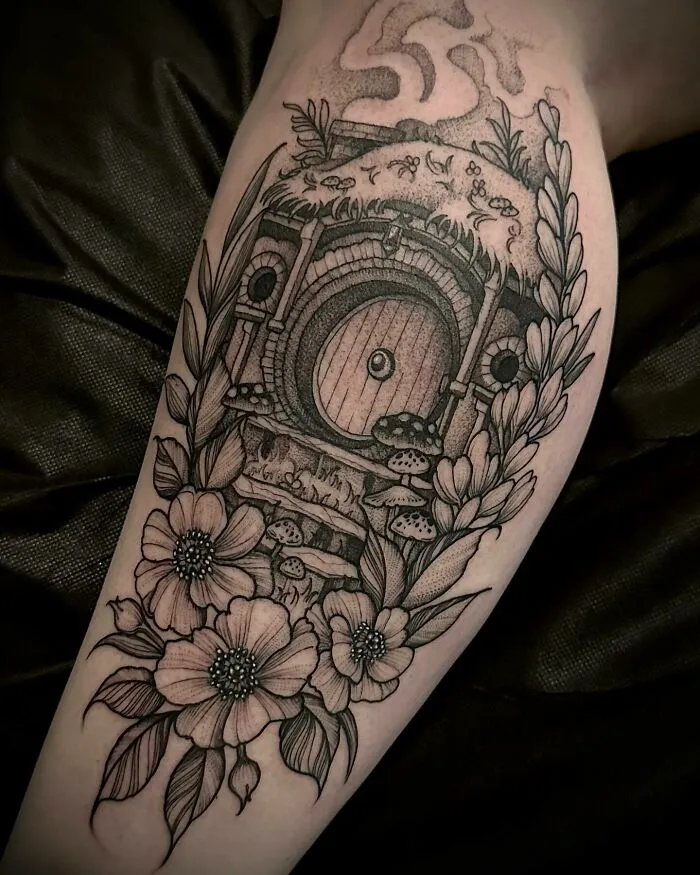 Detailed Lord of the Rings tattoo featuring Hobbit door surrounded by flowers and leaves.