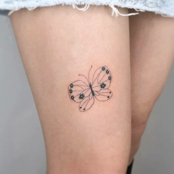 Minimalist butterfly tattoo on thigh, showcasing delicate black ink details.
