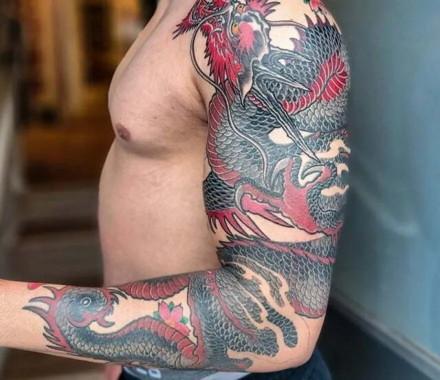 Detailed dragon tattoo covering a man's arm and shoulder, featuring bold red and black ink designs.