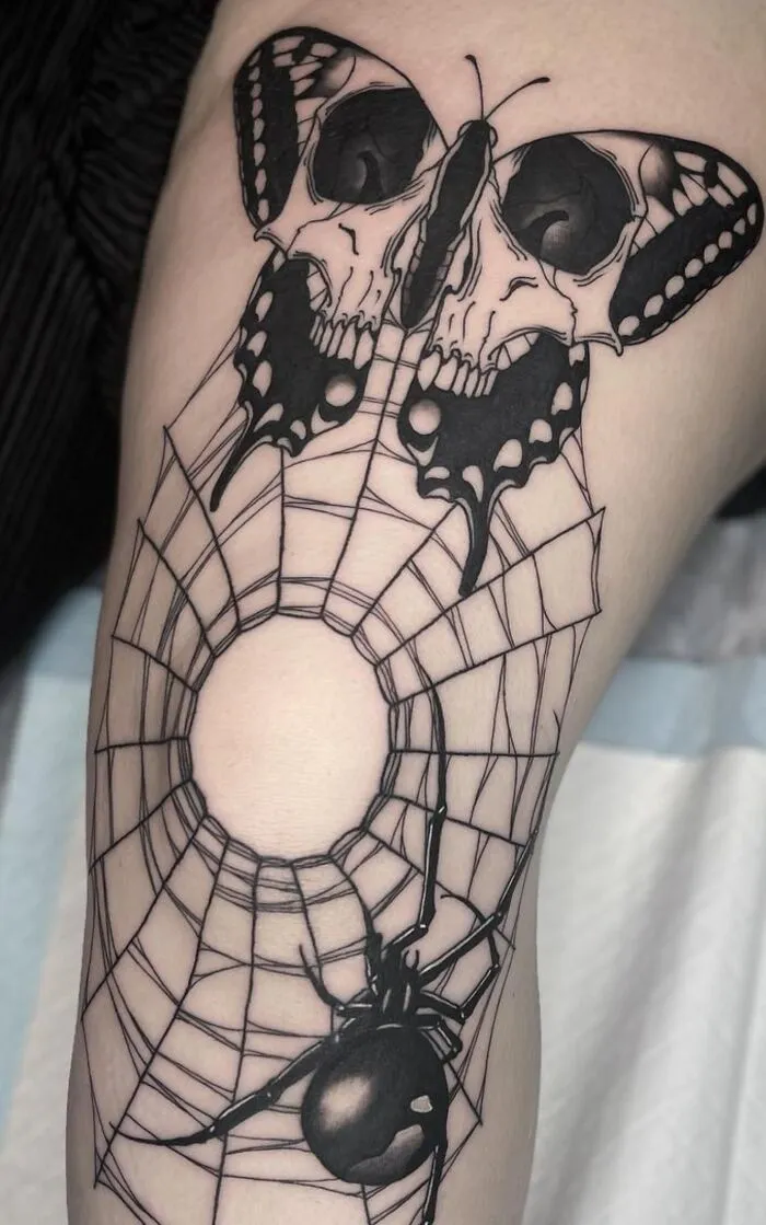 Butterfly tattoo featuring skulls and a spider web, showcasing intricate black ink design.