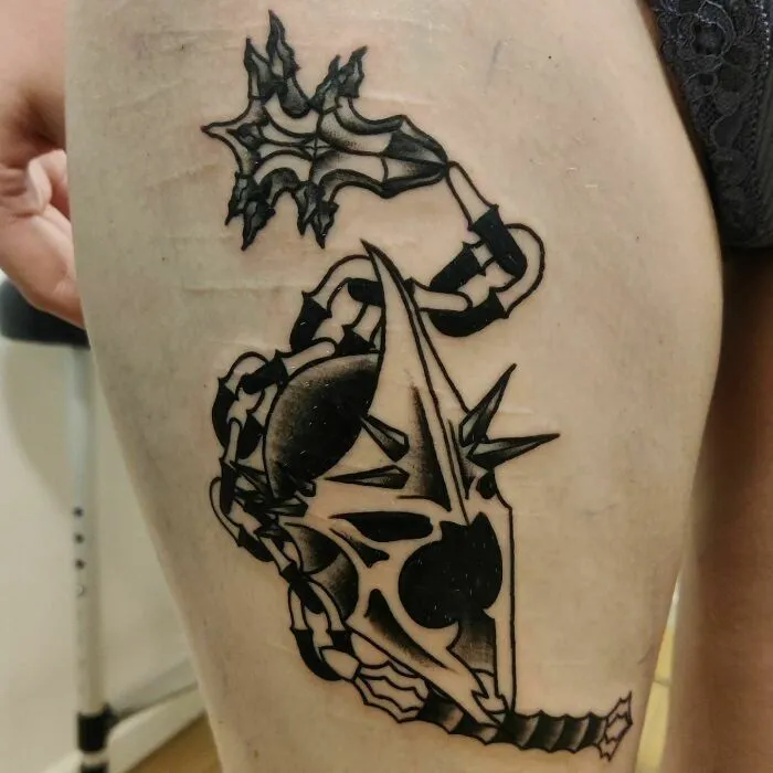 "Intricate tattoo of a helmet featuring spikes and chains inspired by Lord of the Rings on thigh."