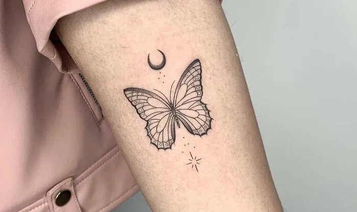 Butterfly tattoo with crescent moon and stars on arm, showcasing intricate line work and shading.