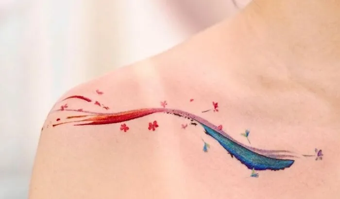 Colorful abstract collarbone tattoo with floral elements on skin.