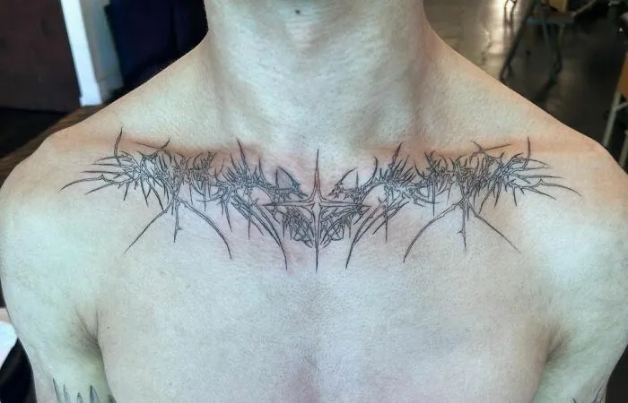 Intricate collarbone tattoo design with fine line details on upper chest of a person.