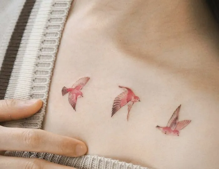 Three pink birds tattooed along a collarbone on a person's skin, showcasing a delicate collarbone tattoo design.