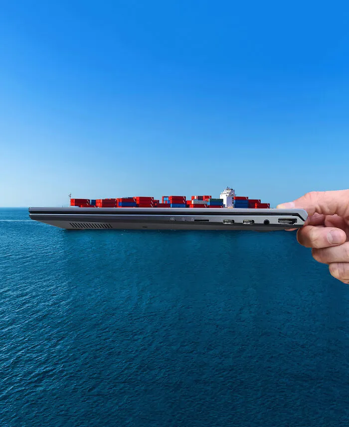 A hand holding a laptop that appears to be a cargo ship, demonstrating how playing with perspective can change what we see.