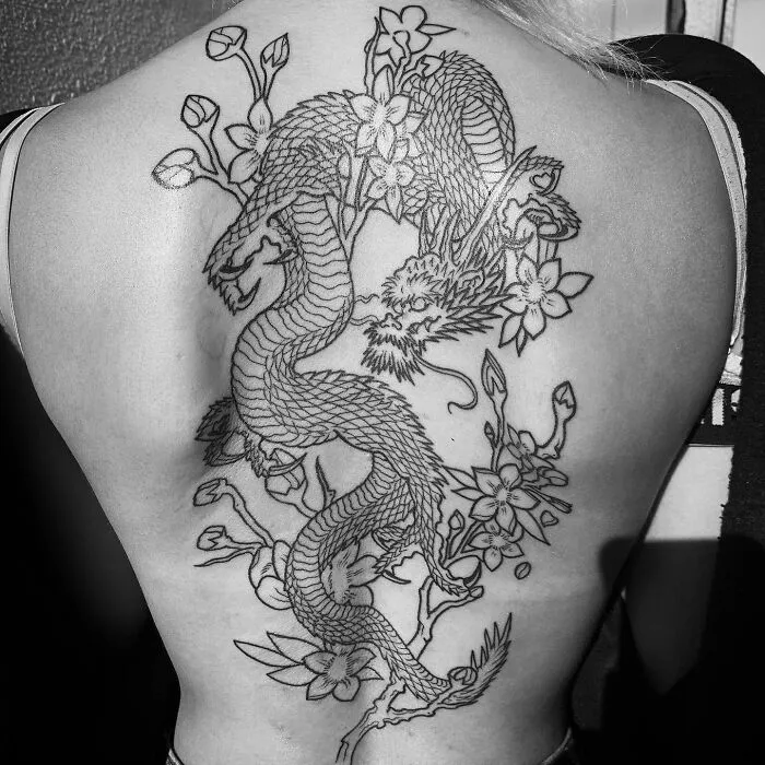 Intricate black ink dragon tattoo design on a person's back, featuring floral elements.