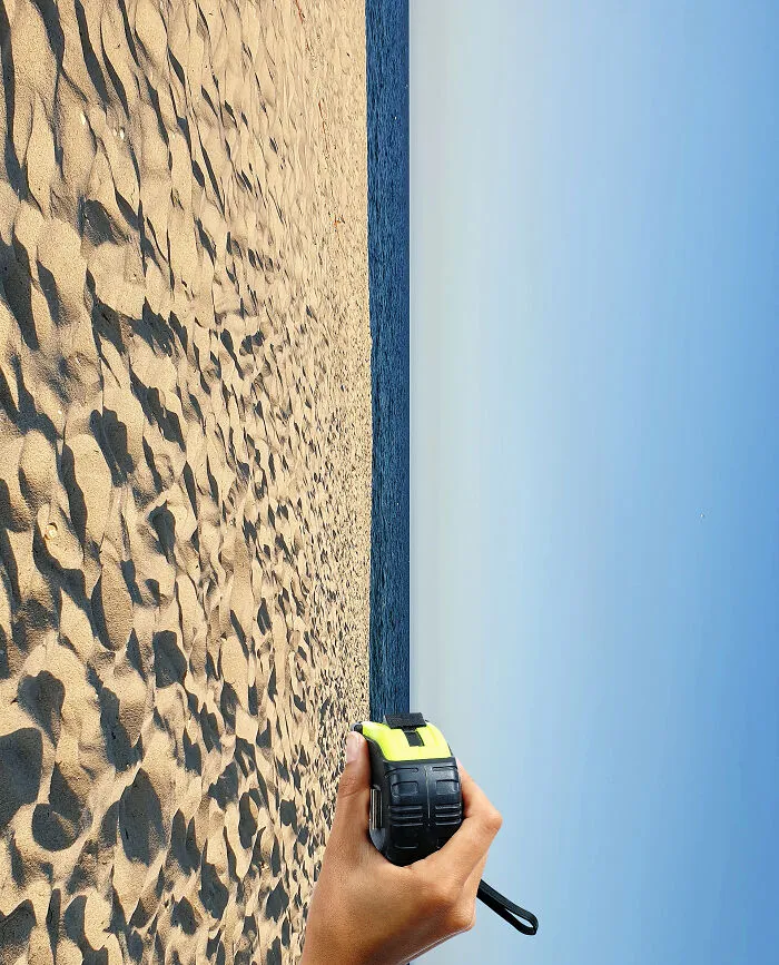 Playing with perspective: A hand holding a tape measure, seemingly measuring the horizon line between a sandy beach and the sky, changing what we see.