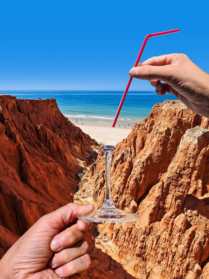Hands hold a glass stem and a red straw against a coastal landscape, showing playing with perspective.