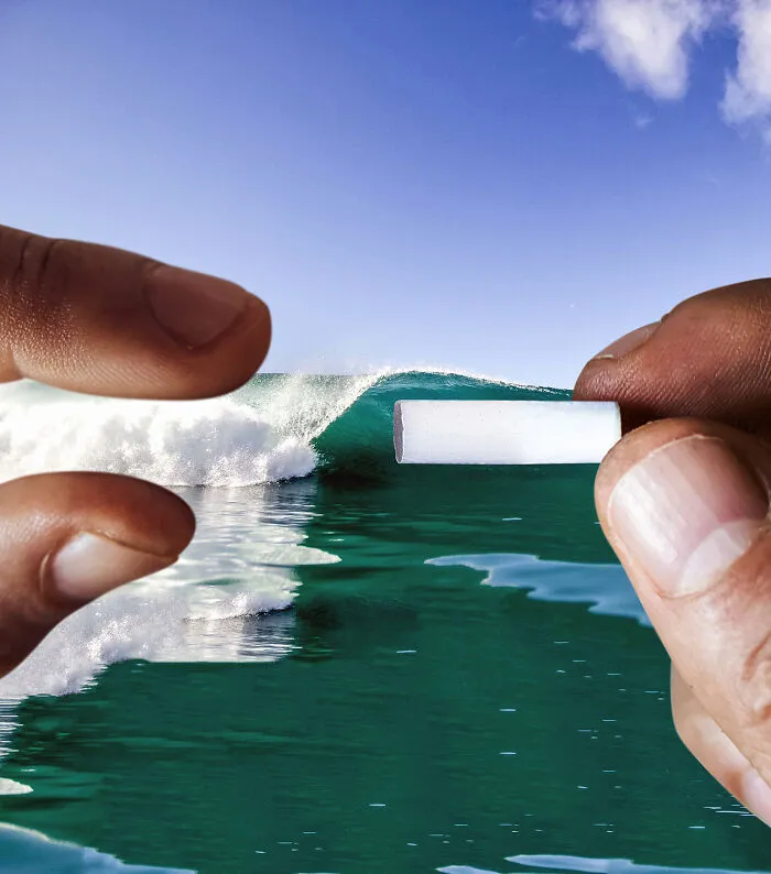 Two hands framing a small white object against a breaking ocean wave, demonstrating how perspective can change what we see.