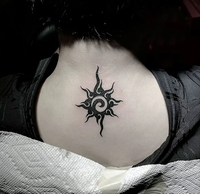 Tribal tattoo on back of neck, showcasing intricate black sun design.