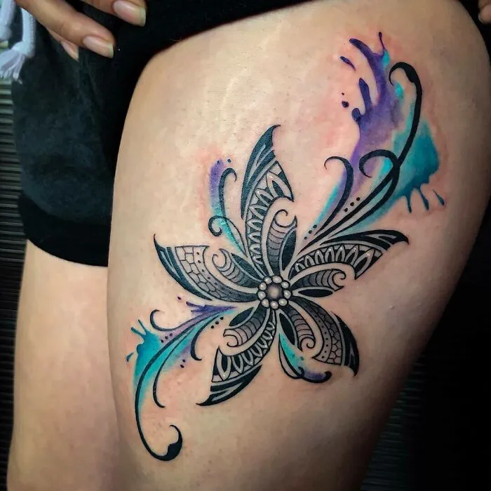 Intricate tribal tattoo design on thigh with floral and swirl patterns in black and colored ink.