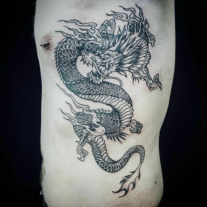 Intricate dragon tattoo design on a person's ribcage, showcasing detailed scales and fierce expression.