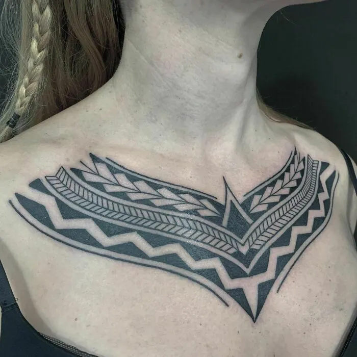 Intricate tribal tattoo on woman's chest featuring geometric patterns and bold black lines.