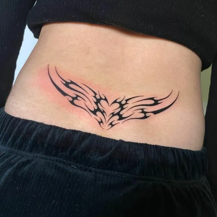 Lower back tribal tattoo with intricate design on a woman wearing black pants.