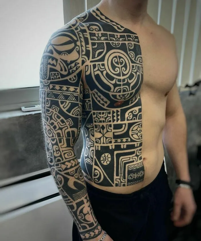 Man showcasing an intricate tribal tattoo sleeve extending to his chest.