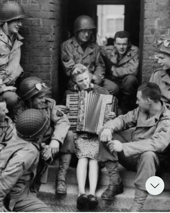 La señora Hale, esposa de un soldado británico, toca el acordeón frente a su casa para un grupo de soldados estadounidenses en Inglaterra, 1944