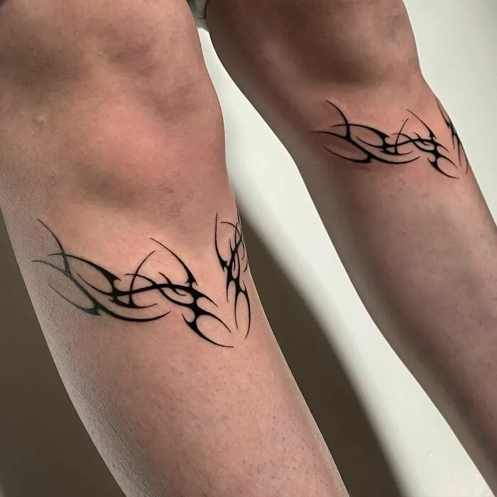 Tribal tattoos on legs with intricate black design and sharp angles, showcasing bold body art.