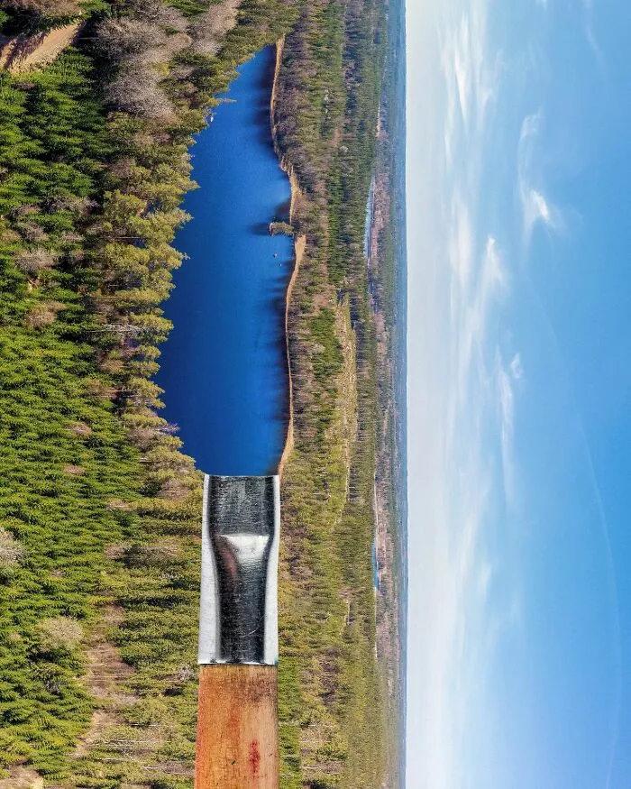 An aerial view of a lake bordered by trees, with the lake shaped like a paintbrush applying blue paint, showing playing with perspective.