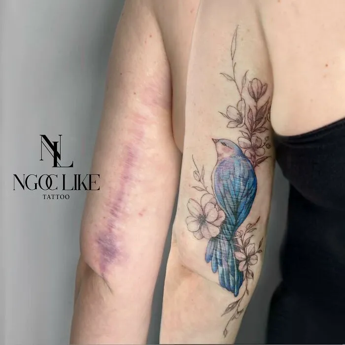 Tattoo artist covers scar with a design of a bluebird and flowers.