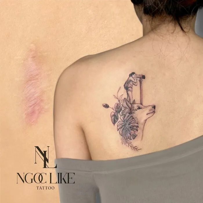 Tattoo art covering scar, featuring a detailed design with flowers and a figure looking through a telescope.