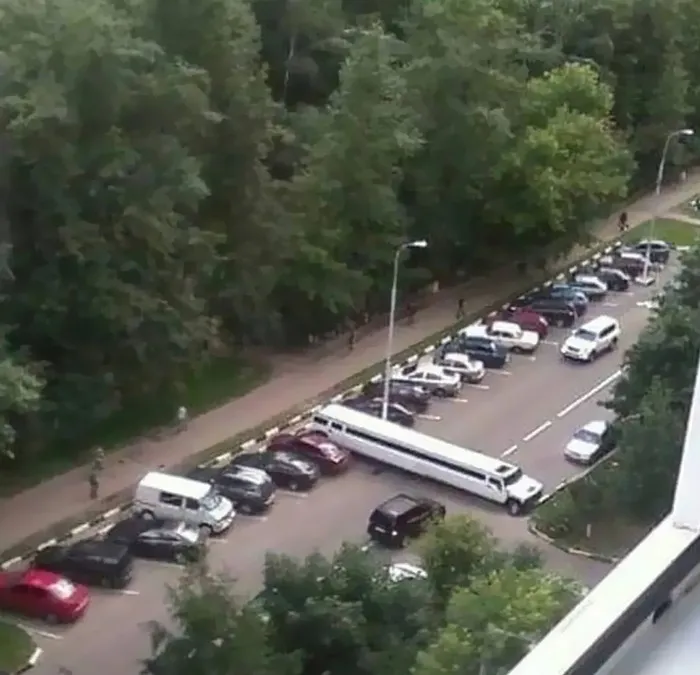 Cursed meme of a long white car awkwardly parked across multiple spaces in a parking lot.