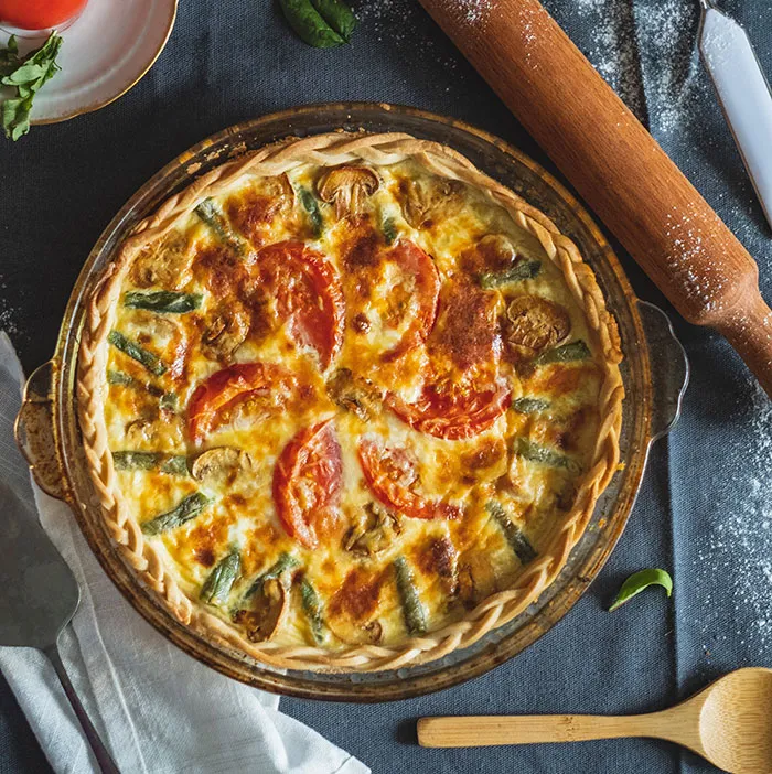 A freshly baked quiche with tomatoes and asparagus, showcasing the flavorful food history of savory pies.