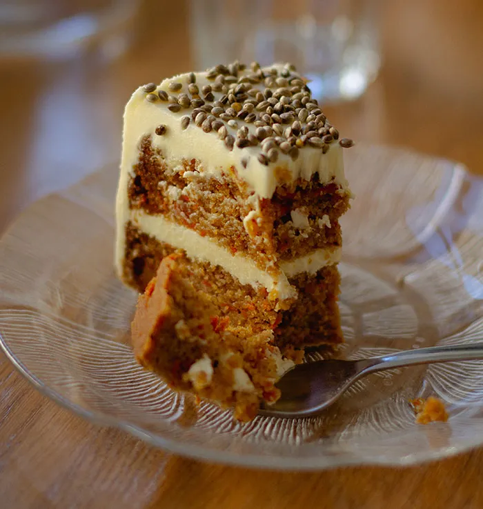 A slice of carrot cake with white frosting and seeds on top, with a bite taken out, illustrating food history facts.
