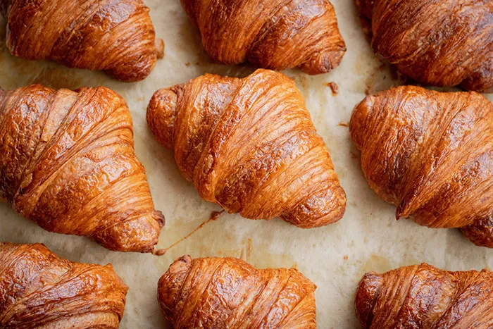 Rows of golden-brown croissants on parchment paper, illustrating delicious food history facts.