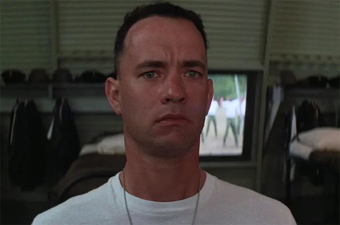 Forrest Gump wearing a white t-shirt looking thoughtful in a military barracks scene for Forrest Gump quotes.